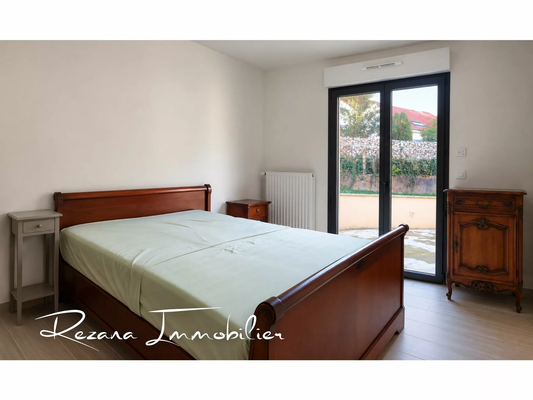 Chambre avec lit en bois et porte-fenêtre donnant sur la terrasse à Héricy.