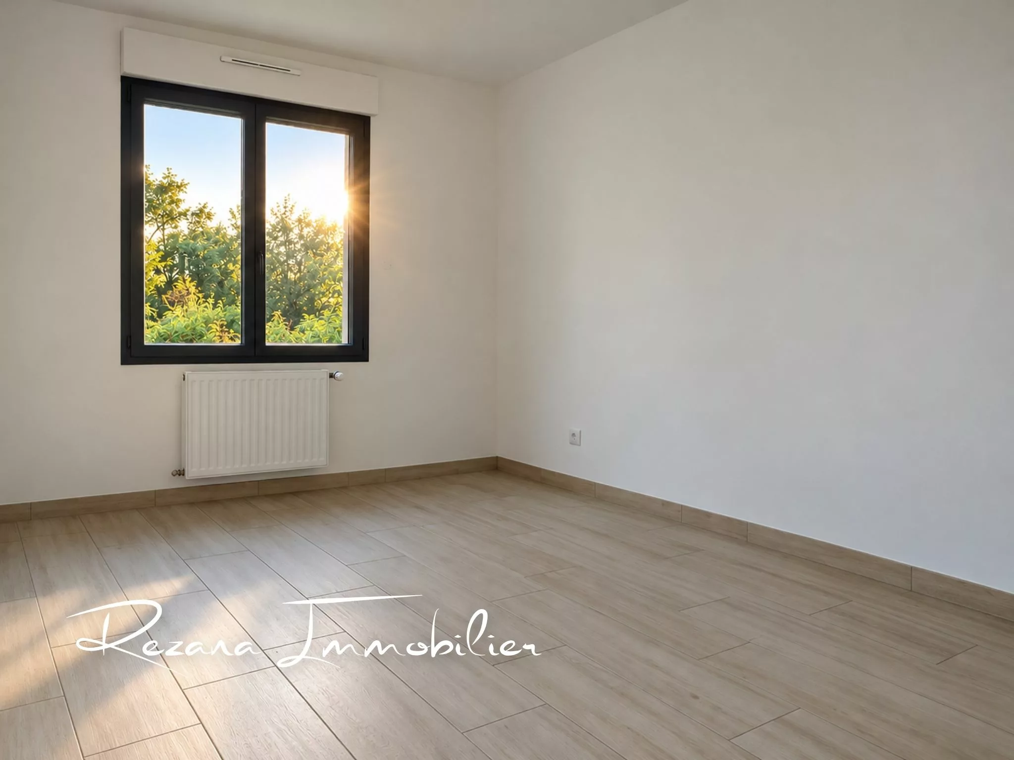 Chambre vide aux murs blancs avec fenêtre et revêtement de sol clair.
