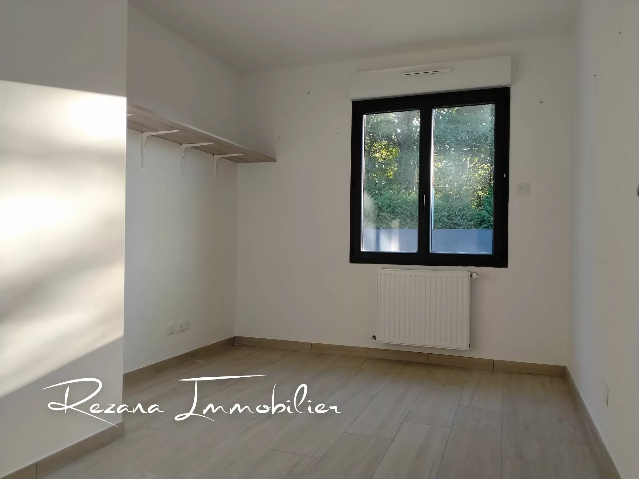 Chambre vide aux murs blancs avec fenêtre et revêtement de sol clair.